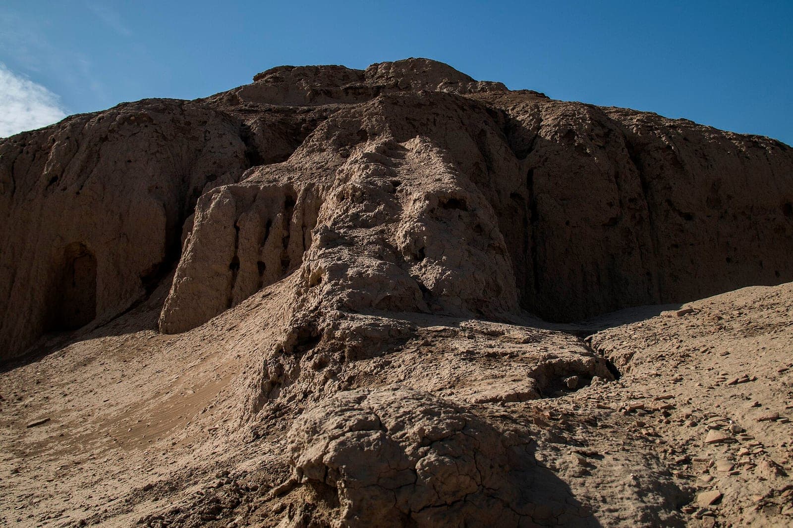 The eroded mud-brick mound of the Eanna ziggurat at Uruk rising against a clear blue sky, with no people or buildings in view.